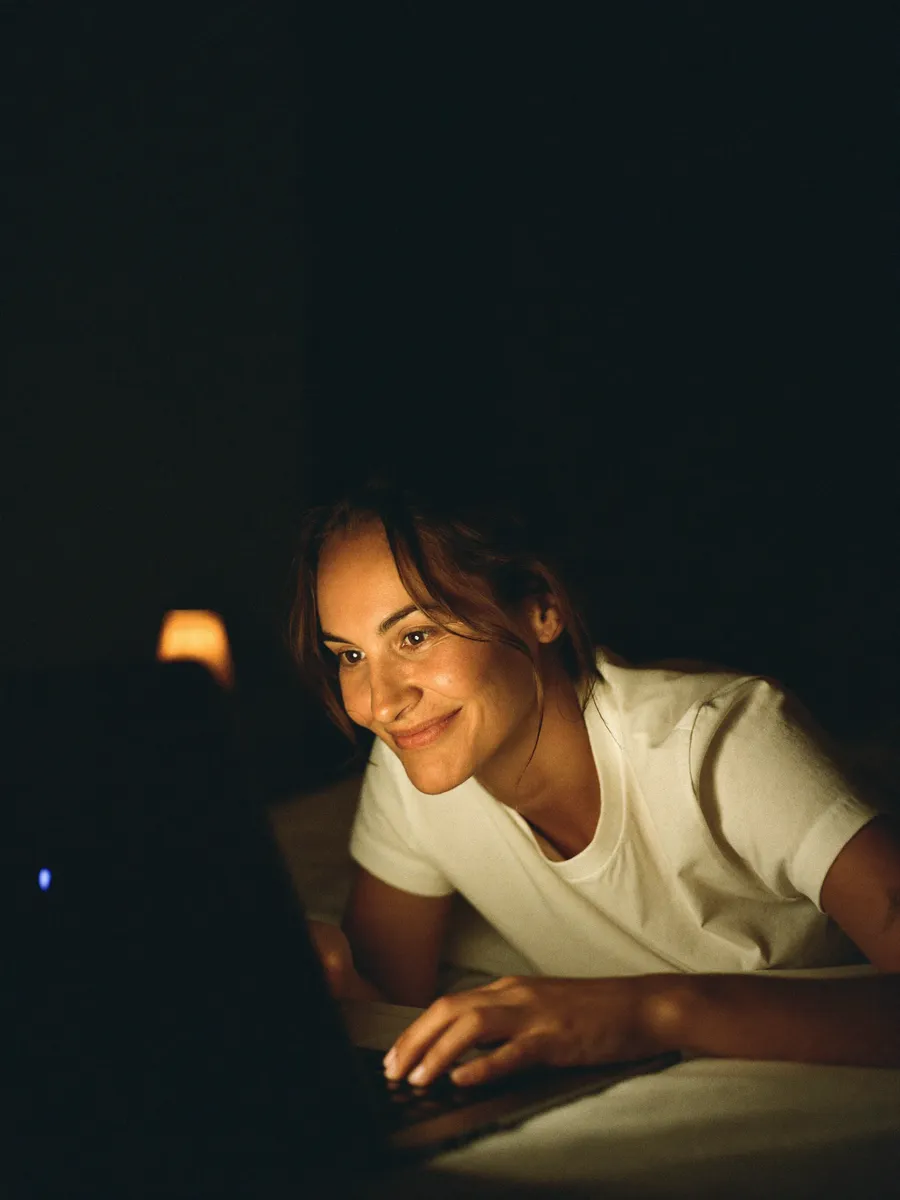 A woman lying in bed late at night, messaging a gym's website on her glowing laptop.