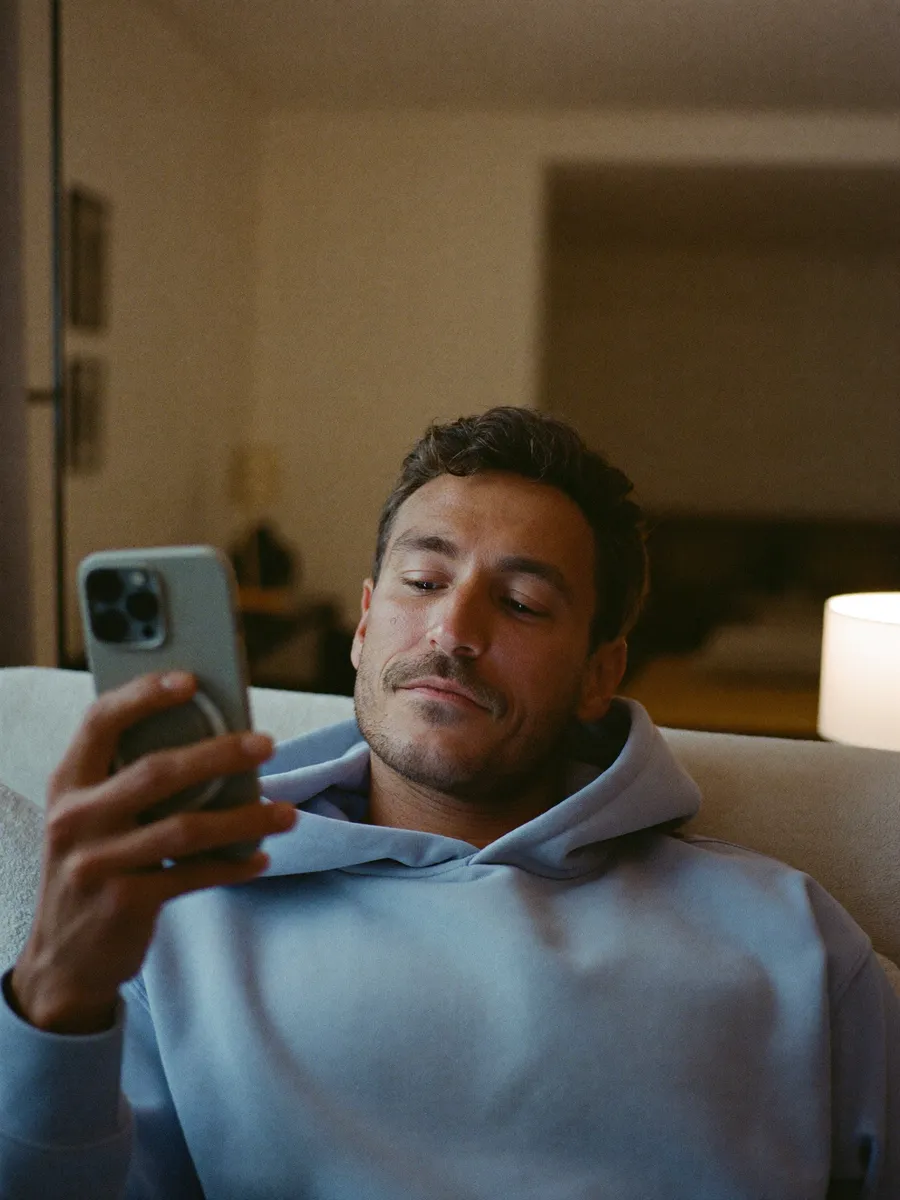 A man relaxing on his couch in the evening, booking a gym trial on his phone.